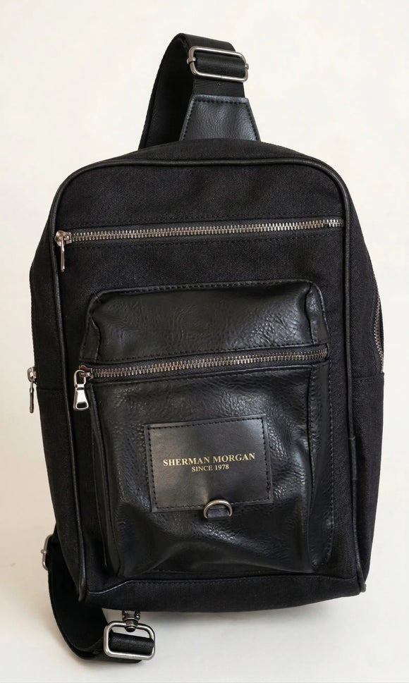 Mochila pechera crossbody Sherman Morgan negra en lona y vinipiel, bolso de hombro tipo sling con múltiples cierres frontales y correa ajustable.
