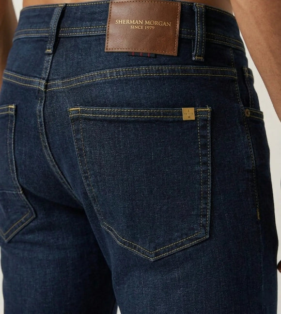 Vista posterior de jeans para hombre con etiqueta de marca en vinipiel café, placa metálica distintiva y bolsillo liso.
