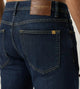 Vista posterior de jeans para hombre con etiqueta de marca en vinipiel café, placa metálica distintiva y bolsillo liso.