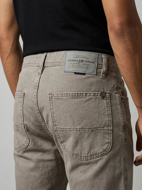 Vista posterior de jeans para hombre con etiqueta de marca en vinipiel gris, placa metálica distintiva y bolsillos con diseño de franja horizontal.