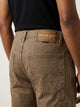 Vista posterior de jeans para hombre con etiqueta de marca en vinipiel café, placa metálica distintiva y bolsillos con diseño de franja horizontal.