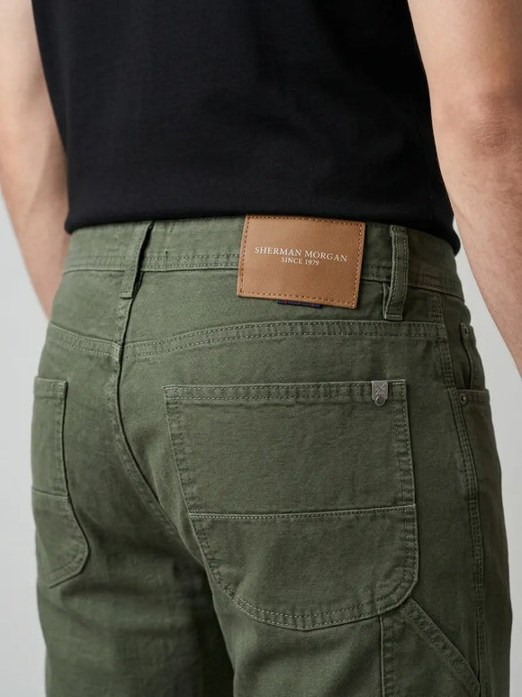 Vista posterior de jeans para hombre corte carpintero con etiqueta de marca en vinipiel café, placa metálica distintiva y bolsillos con diseño de  franja horizontal.