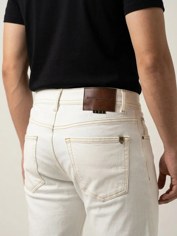 Vista posterior de jeans para hombre con etiqueta de marca en vinipiel café, placa metálica distintiva y bolsillo liso.
