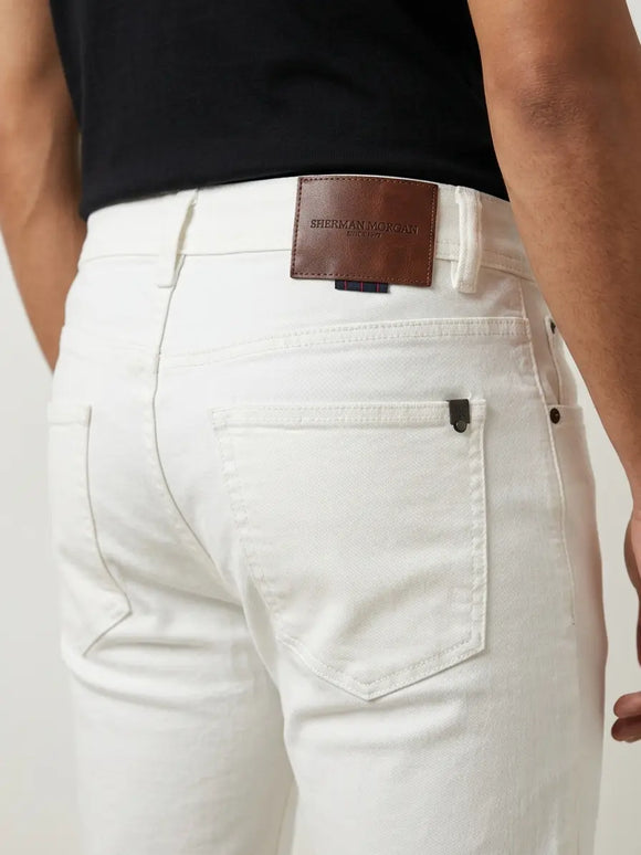Vista posterior de jeans para hombre con etiqueta de marca en vinipiel café, placa metálica distintiva y bolsillo liso.