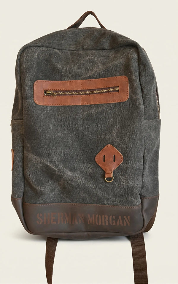 Mochila Sherman Morgan de lona encerada café oscuro con detalles en vinipiel marrón, mochila para hombre de estilo vintage con bolsillo frontal y compartimento lateral.
